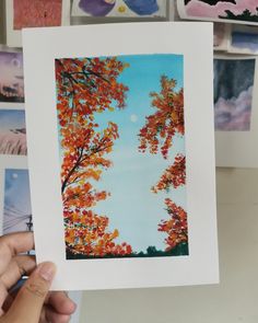 a person holding up a card with trees in the background and pictures on the wall behind them