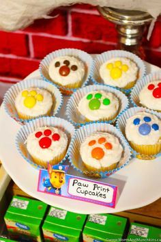 cupcakes with paw prints on them sitting on a plate next to boxes of candy