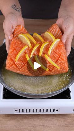 someone is cooking salmon with lemons and onions on the stove top, while holding it in their hands