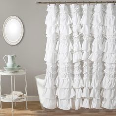 a white shower curtain with ruffles on it in front of a round mirror