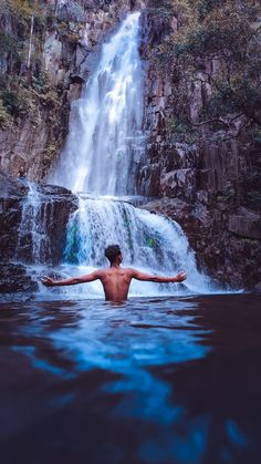 a man standing in the water near a waterfall