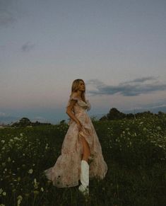 a woman in a long dress and white boots is standing in the middle of a field