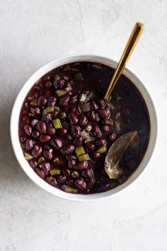 a white bowl filled with beans and green peppers on top of a table next to a spoon