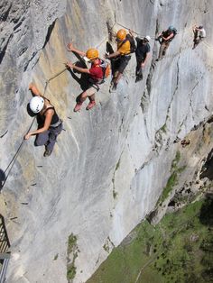 several people climbing up the side of a mountain with helmets on and ropes attached to them