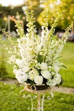 a vase filled with white flowers sitting on top of a metal stand in the grass