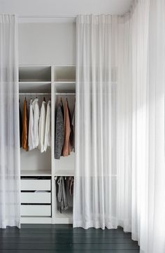 an open closet with white curtains and clothes