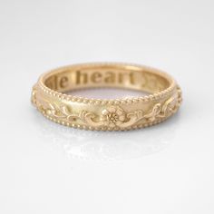 a gold wedding band with the word be heart on it's center and flowers in the middle