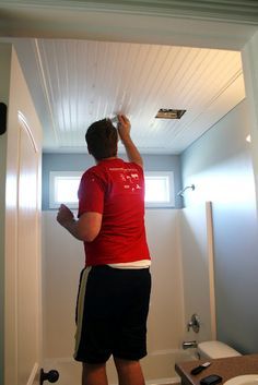 the man is painting the ceiling in the room with white paint and black shorts on