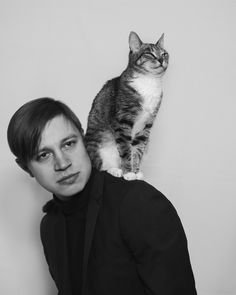 a cat sitting on the back of a man's head while he poses for a black and white photo