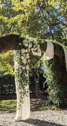 an outdoor wedding setup with white flowers and greenery on the arbor, surrounded by trees