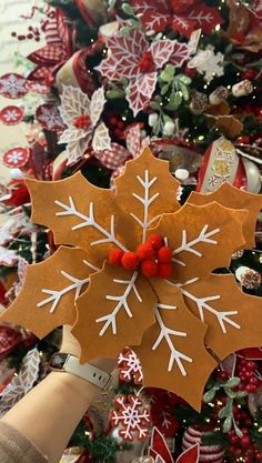 someone is holding up a paper snowflake ornament in front of a christmas tree