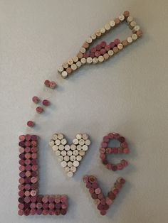 the word love spelled with wine corks in pink, white and grey colors on a wall