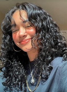 a close up of a person with long curly hair and wearing a blue shirt looking at the camera