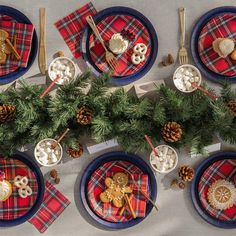 the table is set for christmas dinner with plaid napkins and pine cones on it