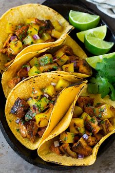 three tacos with meat, pineapple and cilantro on a black plate