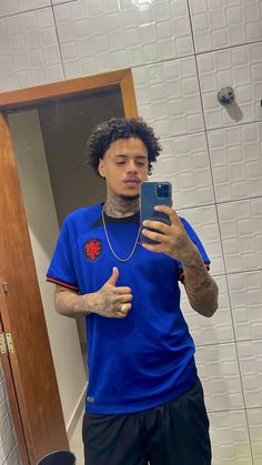 a man with tattoos taking a selfie in the bathroom while wearing a blue shirt and black shorts