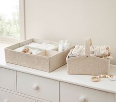 two storage bins sitting on top of a white dresser next to a stuffed animal