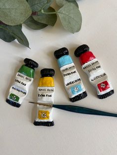 four miniature paint tubes are sitting next to a green plant