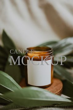 a candle with a label on it sitting next to some green leaves and greenery