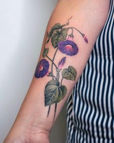 a woman with a tattoo on her arm has a purple flower and leaves growing out of it