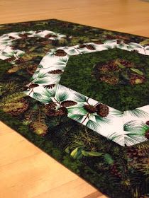 a green area rug with pine cones and evergreen leaves on the center, surrounded by wood flooring