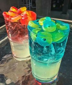 two glasses filled with different colored liquids on top of a glass table next to each other