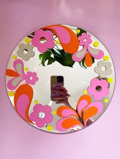 a hand holding a cell phone in front of a mirror with flowers painted on it