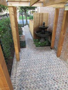 a brick walkway with a fountain in the center between two wooden posts and a fence