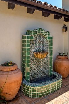 a green and blue fountain sitting on top of a tiled floor next to potted plants