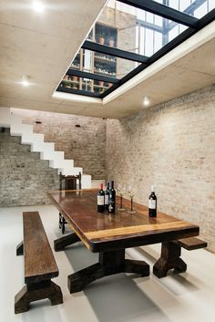 a wooden table sitting under a skylight next to some bottles of wine and two benches