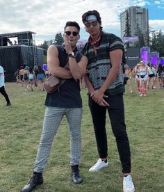 two young men standing next to each other on top of a grass covered field with people in the background