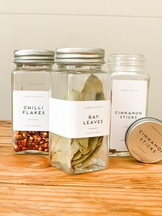 three glass jars filled with spices on top of a wooden table