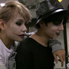 two people with makeup on their faces and one is wearing a black hat while the other wears a white shirt