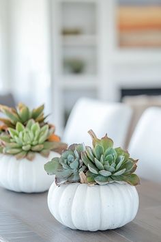 two small white pumpkins with succulents on them sitting on a table