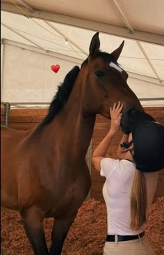 a woman standing next to a brown horse under a white tent and touching it's head