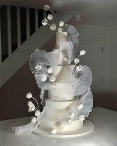 a white wedding cake with flowers on top is sitting on a table in front of stairs