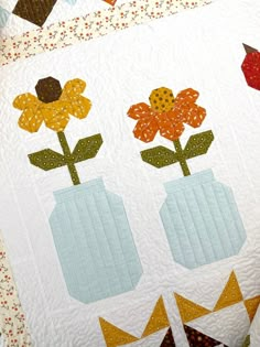 two vases with flowers in them on a quilt