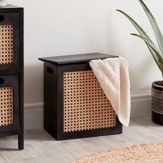 two black and brown baskets on the floor next to a potted plant with a white towel