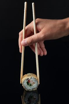 a hand holding two chopsticks over a sushi roll on a black surface