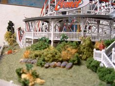 a miniature model of a roller coaster with trees and bushes in front of the ride