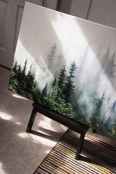 an easel is sitting on the floor in front of a painting that looks like a forest