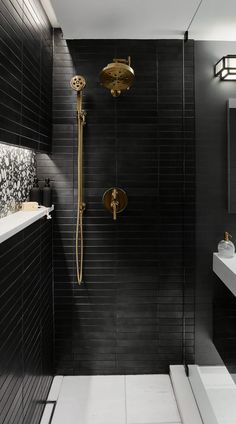 a black tiled bathroom with gold fixtures and white counter tops, along with a walk in shower