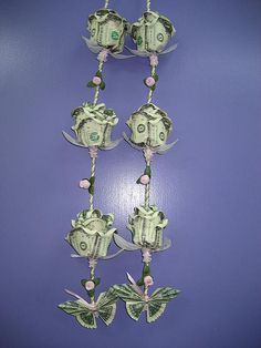 dollar bills are attached to a string with flowers and butterflies hanging from the ends on a purple wall