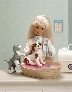 a barbie doll sitting on top of a bed next to two dogs and a cat