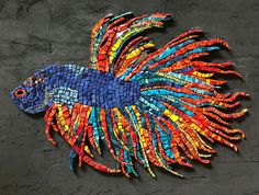 a colorful fish made out of small pieces of colored paper on a black surface with grey background