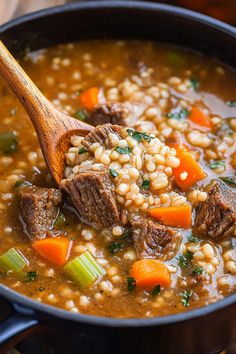 a pot filled with beef and barley soup on top of a wooden spoon in it