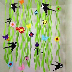 paper flowers and bugs are hanging from the ceiling in front of a wall with green grass