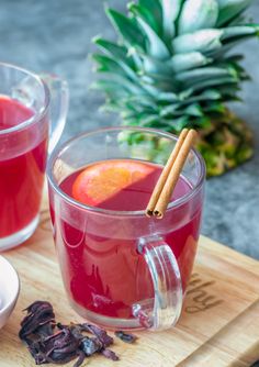 two glasses filled with red liquid next to a pineapple