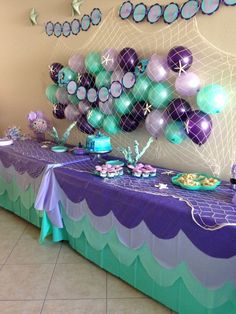 the table is set up with purple and green balloons on it, along with other decorations