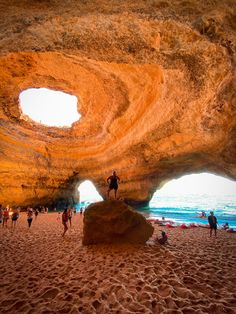 people are walking on the beach near an arch shaped formation in the sand and water